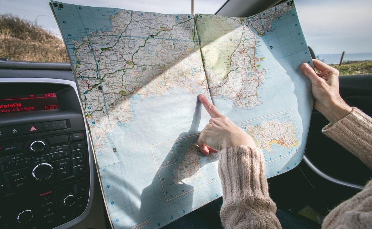 Persona dentro de un auto señalando una ubicación en un mapa desplegado, planificando una ruta de viaje.